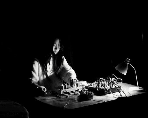 A person is working with electronic equipment on a dimly lit table, with a desk lamp illuminating the scene.